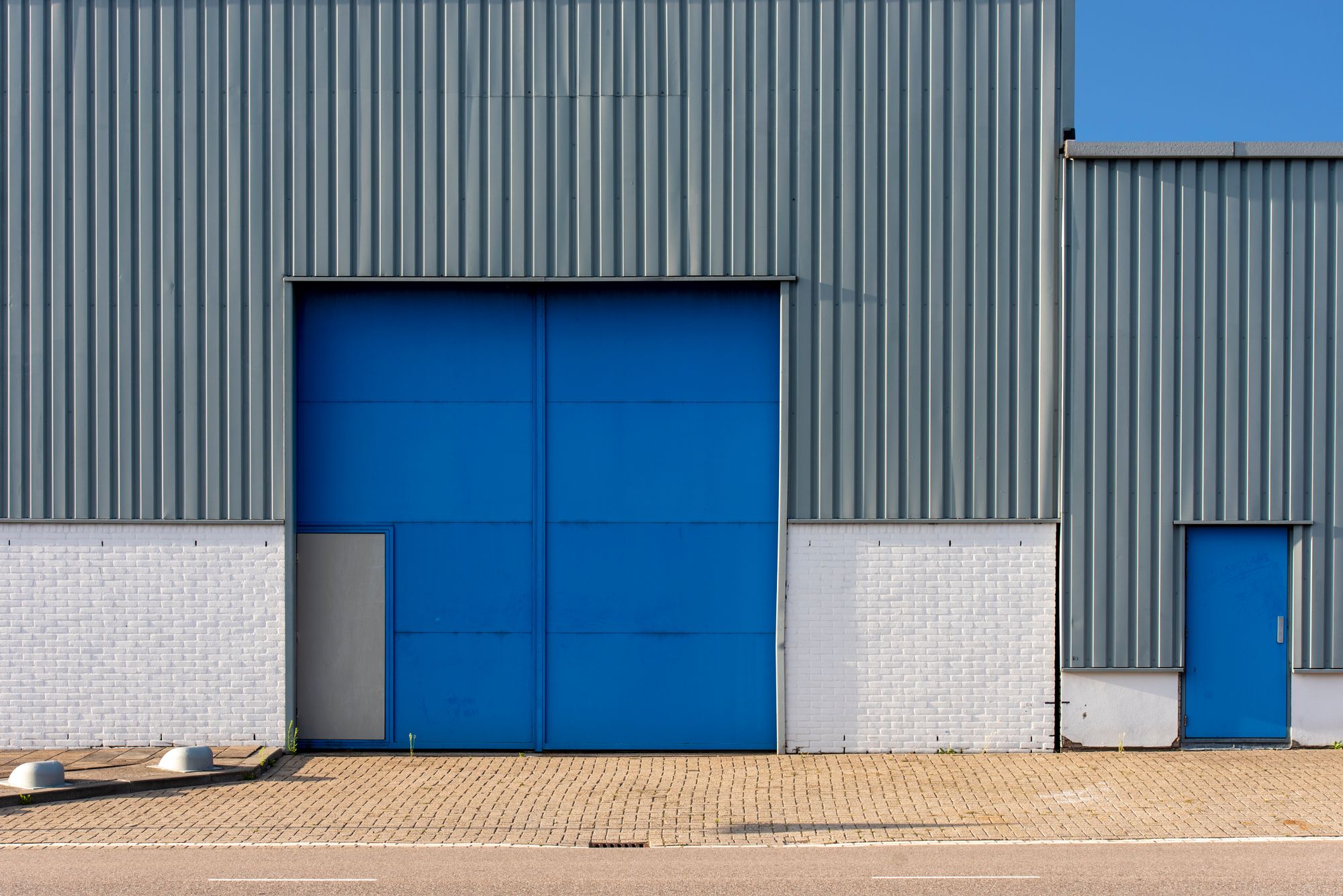 Illustrative photograph of a metal warehouse facade with a blue door. Not a completed company project.